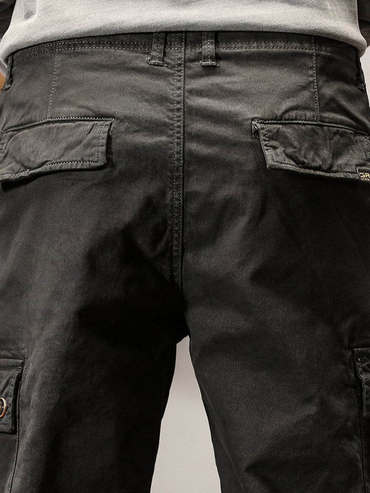 Un homme porte un pantalon cargo noir avec des poches cargo sur les côtés. Coupe droite pour un look masculin intemporel. Disponible en tailles US 28 à 38. Confortable et stylé.