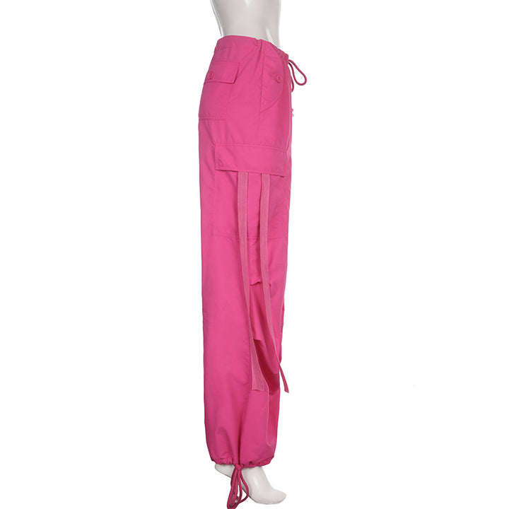 Un mannequin porte un pantalon rose baggy à taille basse avec des lanières pendantes, créant une silhouette unique et audacieuse. Disponible en tailles S à L, ce pantalon cargo pour femme offre un confort inégalé grâce à sa coupe large façon parachute et à sa texture douce et extensible en polyester, jersey et spandex. Les chevilles élastiques ajoutent à l'effet baggy, tandis que la couleur rose apporte une touche de fraîcheur. Parfait pour un style street féminin.