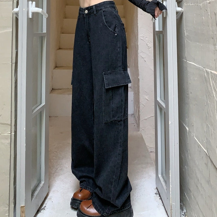 Une personne debout dans une porte, portant un jean cargo large taille haute noir. Le jean a une coupe large avec des poches cargo fonctionnelles. Disponible du S au XL.