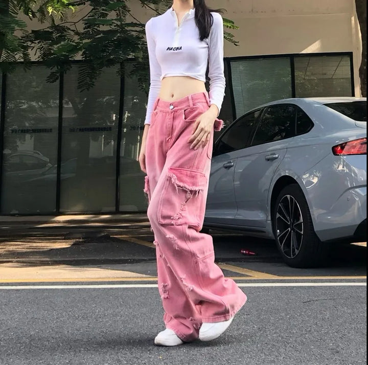 Une femme debout devant une voiture, portant un jean cargo baggy rose délavé avec des déchirures judicieusement placées. Taille haute pour une silhouette moderne. Un look audacieux des années 2000, ajoutant une touche d'insouciance et de féminité. Disponible en tailles XS à XL.