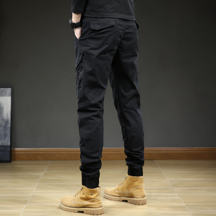 Un homme porte un pantalon cargo slim resserré aux chevilles de couleur noir. Le pantalon est confortable et élégant avec une coupe moderne. Disponible en tailles US 28 à 38.