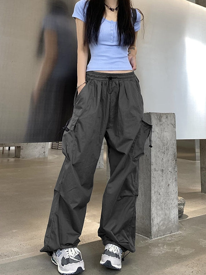 Une femme portant un pantalon cargo baggy léger gris, avec une coupe confortable et des élastiques à la taille et aux chevilles. Le pantalon est doté de poches latérales pour un look street et féminin. Disponible en tailles S à 3XL.