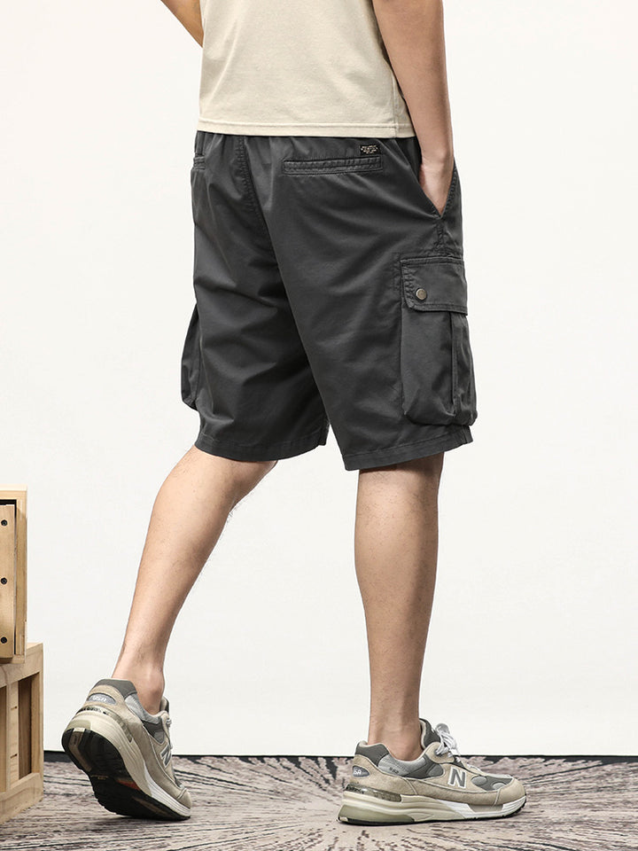 Un homme portant un short cargo gris coupe droite et des sneakers. Les poches latérales à boutons-pression ajoutent une touche pratique à ce short au style masculin et militaire.