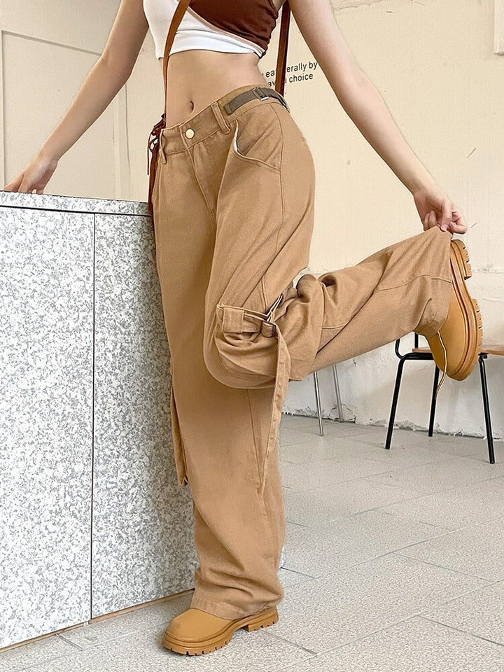 Une femme porte un jean cargo baggy camel avec des lanières aux poches. Ce jean taille haute offre un look urbain tendance. Disponible du S au L.