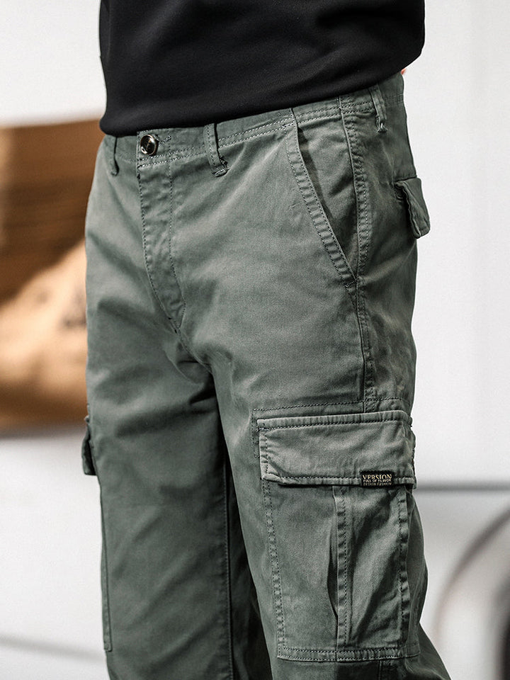 Un homme porte un pantalon cargo gris avec des poches cargo sur les côtés. Coupe droite pour un look masculin intemporel. Disponible en tailles US 28 à 38. Confortable et stylé.