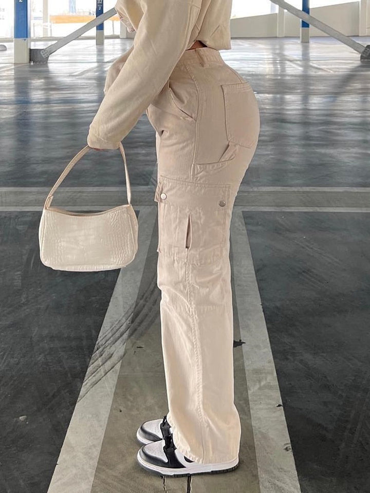 Femme en combinaison blanche ajustée, tenant un sac à main. Pantalon cargo taille haute beige pour un look féminin et urbain. Coupe évasée, convient à toutes les morphologies. Confectionné en coton pour un confort maximum. Disponible du S au XL.