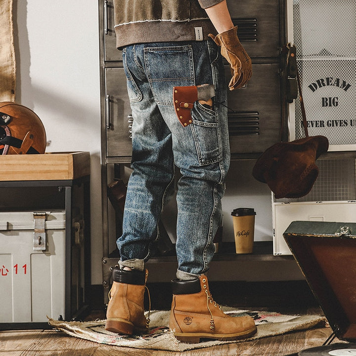 Un homme portant des gants en cuir et un jean cargo délavé coupe droite - Bleu. Les poches latérales ajoutent une touche tendance à cette tenue. Disponible en tailles US du 28 au 40, ce jean en 100% coton offre un confort durable.