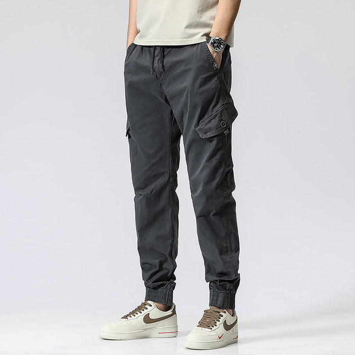 Un homme portant un pantalon cargo gris avec fermeture rouge et des baskets blanches