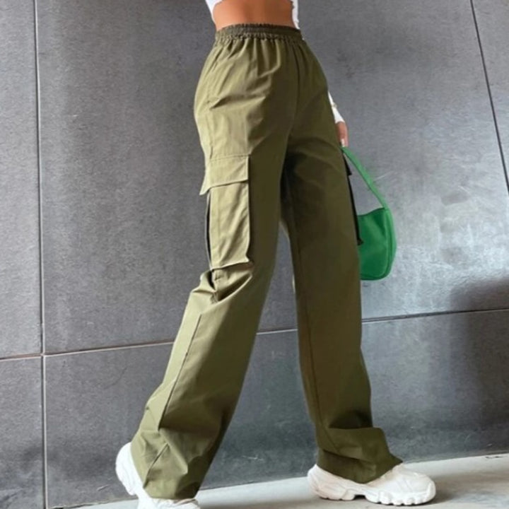 Une femme porte un pantalon cargo baggy kaki avec taille haute et jambes larges. Le pantalon est en 100% polyester pour une légèreté et une durabilité optimales. Les multiples poches sur les jambes ajoutent un côté fonctionnel à ce pantalon unique. Disponible du S au XL.