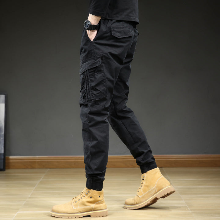 Un homme portant un pantalon cargo slim resserré aux chevilles, avec des bottes jaunes. Confortable et élégant, ce pantalon noir est en coton et élasthanne. Tailles disponibles : 28 à 38 (US).