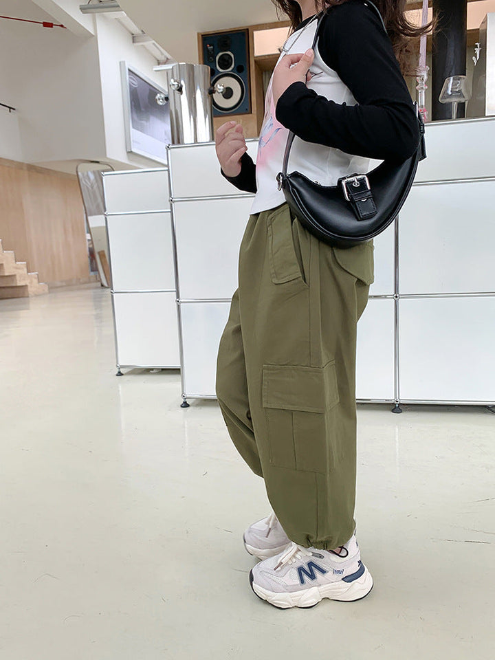 Une personne debout dans une pièce, portant un Pantalon cargo jogger large kaki avec des poches latérales pratiques et resserré aux chevilles. Le pantalon est disponible du 2 au 7 ans et allie confort et style urbain.