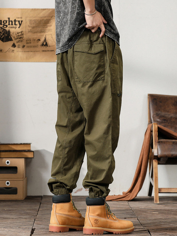 Un homme porte un pantalon cargo kaki ample et léger, parfait pour l'été. Coupe droite, avec des poches fonctionnelles sur les côtés. Tailles disponibles du M au 3XL. Matières : 97,5% coton + 2,5% Spandex pour un confort aéré et une flexibilité accrue.