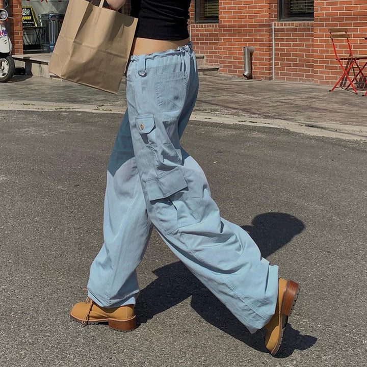 Une personne marchant avec un sac, portant un pantalon cargo baggy taille basse élastique bleu ciel pour femme.
