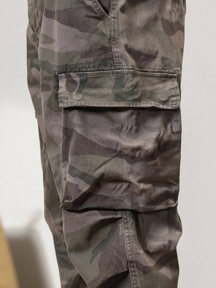 Un pantalon cargo gris camo coupe large resserré aux chevilles pour homme. Style militaire avec poches. Confortable et durable en coton. Tailles US 28 à 38.