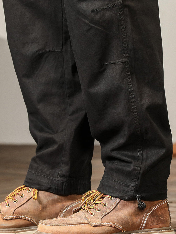 Un homme porte des chaussures marron, un pantalon cargo léger ample coupe droite noir pour homme. Les poches sur les côtés ajoutent une touche fonctionnelle.