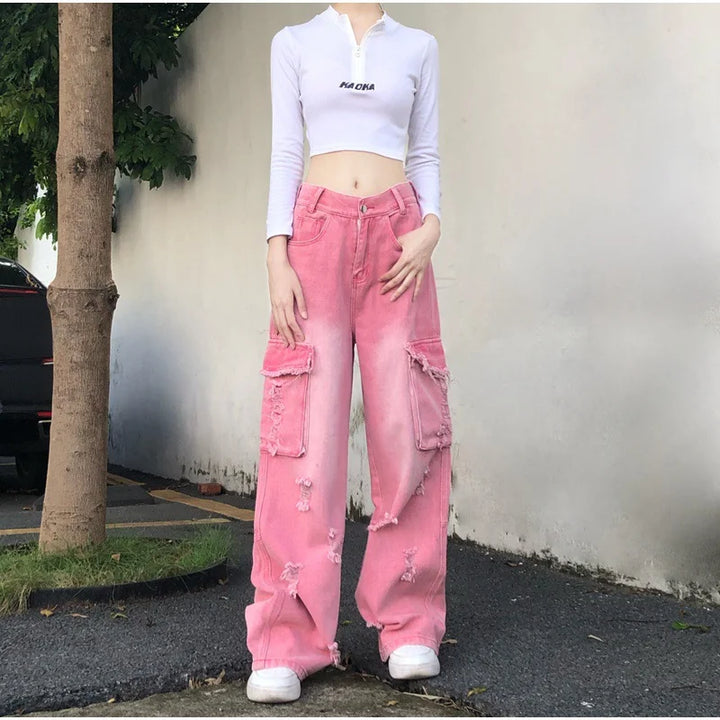 Une personne portant un pantalon rose délavé avec déchirures judicieusement placées, taille haute. Un jean cargo baggy rose délavé pour femme, revisitant l'audace des années 2000. Un look iconique du streetwear pour celles qui osent défier les conventions avec style. Tailles disponibles du XS au XL.