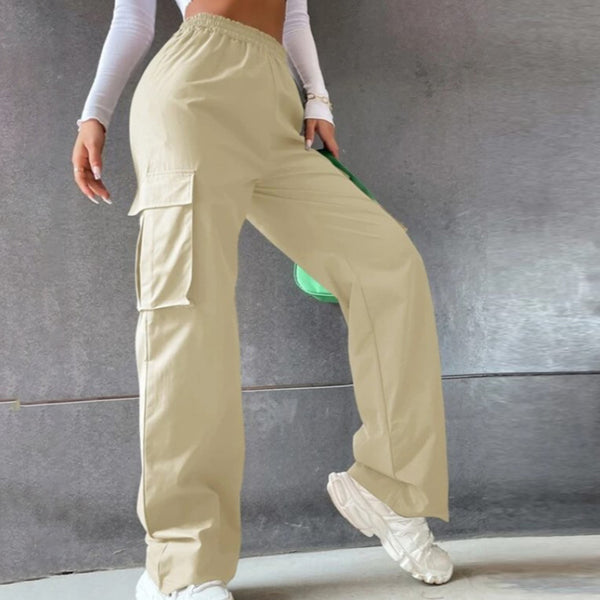 Une femme porte un top bustier à manches longues blancs, des baskets blanches, un sac vert et un pantalon cargo baggy beige à taille élastique haute.