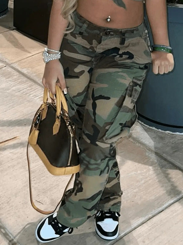 Une femme pose dans la rue avec des baskets blanches et noires, un sac à main de luxe. Elle porte aussi un pantalon cargo kaki avec motif camo. La coupe est ajustée et légèrement évasé en bas.