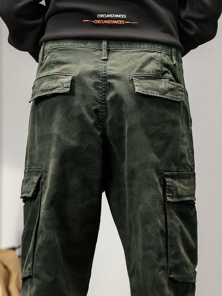Un homme portant un pantalon cargo kaki, coupe large resserré aux chevilles. Style masculin avec une touche militaire. Confortable et durable, en 100% coton. Disponible en tailles US 28 à 38.