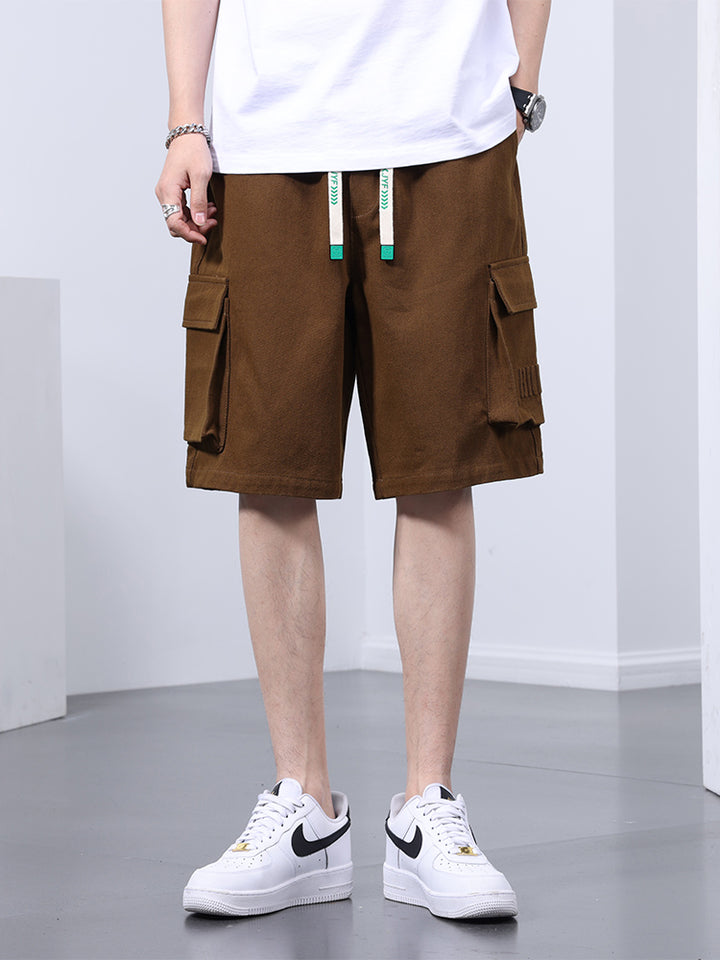 Un homme portant un short cargo marron, des sneakers blanches. Coupe large pour un style street décontracté. Disponible en tailles M à 8XL. Conçu en coton et viscose pour un confort optimal et une grande liberté de mouvement.