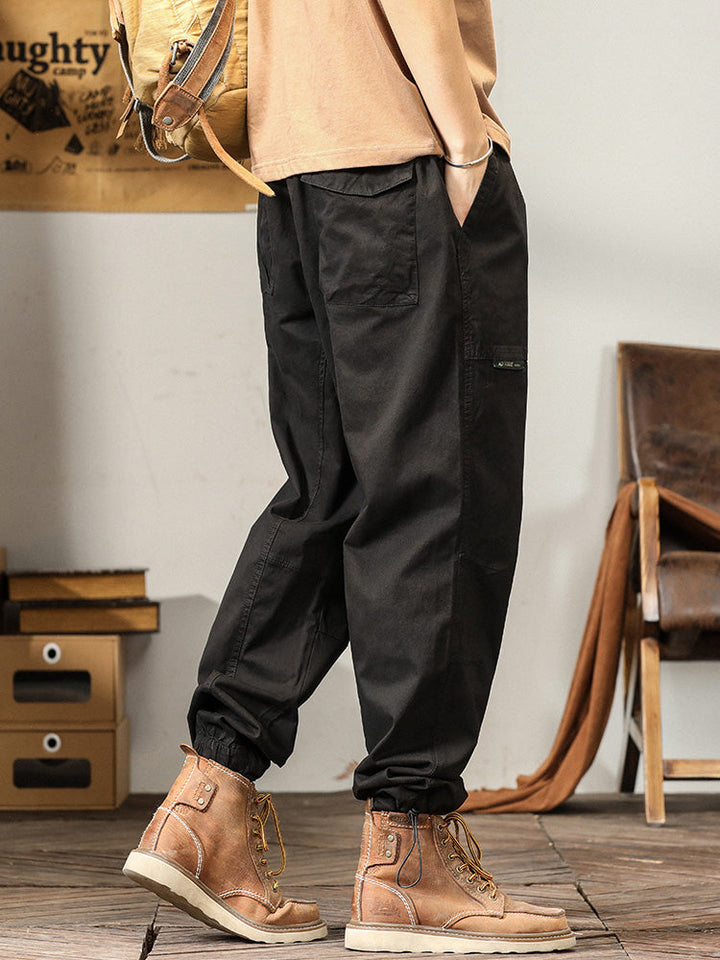 Un homme portant des bottes marron et un pantalon noir ample avec des poches cargo. Les bottes et le pantalon sont disponibles sur Cargo District, un site de vente de vêtements de style cargo.