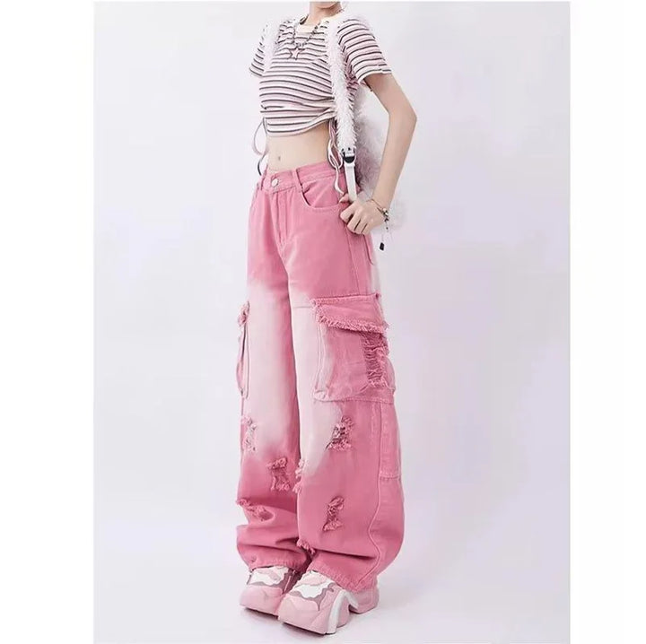 Une femme portant un jean cargo baggy rose délavé avec des déchirures judicieusement placées et une taille haute. Un look audacieux des années 2000 pour celles qui osent défier les conventions avec style. Disponible en tailles XS à XL.