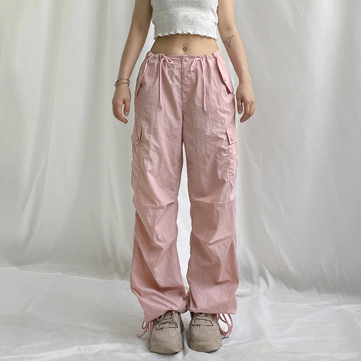 Une personne portant un pantalon cargo rose avec une taille basse et un style baggy. Le pantalon a une jambe large avec un élastique à la cheville pour un confort optimal. Disponible du S au L. Matières : Polyester, Spandex. Cargo District, site de vente de vêtements de style cargo.