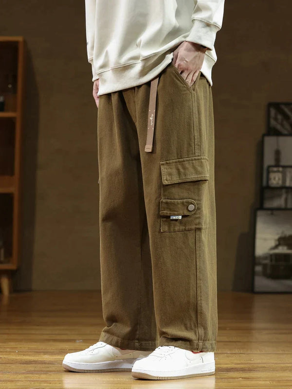 Un homme porte un pantalon cargo ample en coton noir avec une ceinture intégrée. Parfait pour la vie urbaine, ce pantalon offre une durabilité exceptionnelle et une liberté de mouvement optimale. Disponible dans une large gamme de tailles, du M au 8XL.