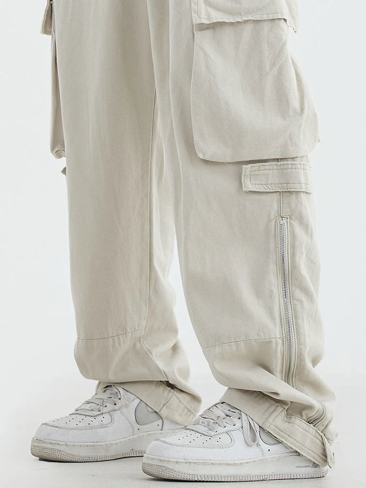 Un homme porte un pantalon blanc et des baskets blanches. Le pantalon est ample avec des poches et une fermeture éclair. Le style est décontracté et inspiré du streetwear japonais.