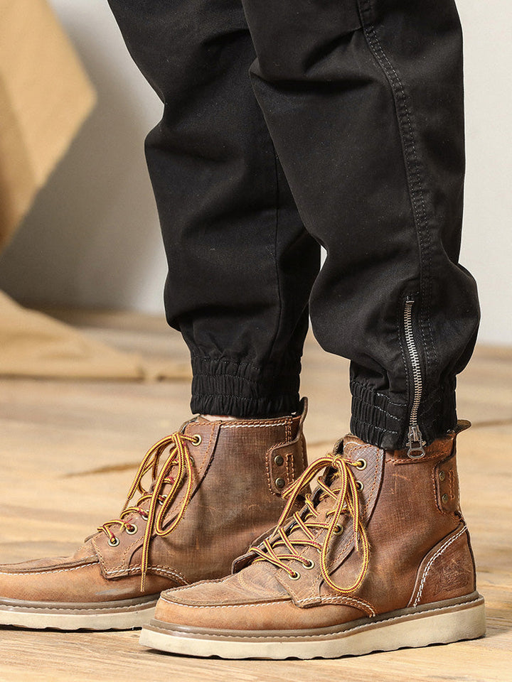 Un homme porte des bottes marron avec lacets jaunes, assorties au pantalon cargo coupe droite à poches à bouton noir. Le pantalon est confortable et flexible grâce à sa composition en 97% coton et 3% Spandex. Disponible en tailles US 28 à 38.