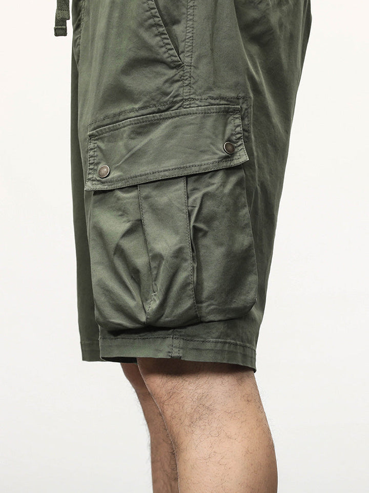 Un homme porte un Short cargo coupe droite kaki avec des poches latérales à boutons-pression. Fabriqué à partir de 95% coton et 5% spandex, ce short offre confort et élasticité. Tailles disponibles du 28 au 40.