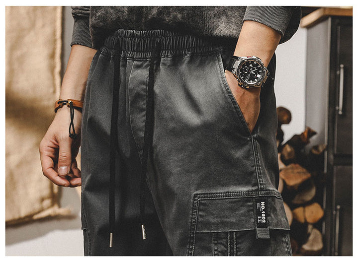 Un homme porte une montre en cuir noir - Pantalon cargo ample à coutures resserré aux chevilles - Noir - Homme, Cargo District.