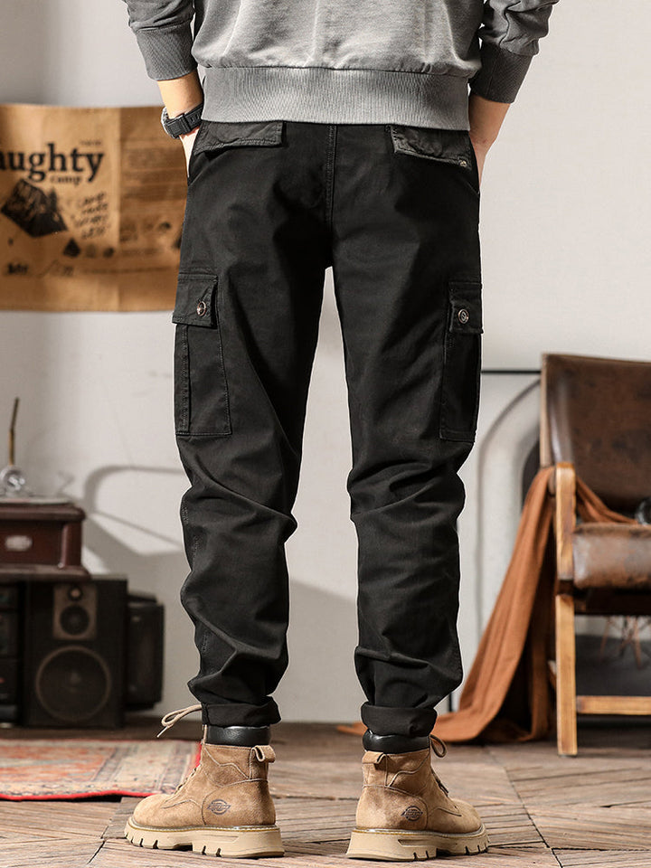 Un homme portant un pantalon cargo noir avec des poches cargo sur les côtés. Coupe droite pour un look masculin intemporel. Disponible en tailles US 28 à 38. Confortable et stylé.