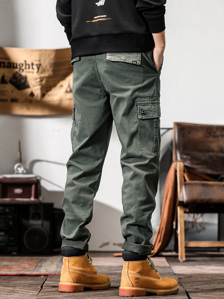 Un homme porte un pantalon cargo gris avec des poches cargo sur les côtés. Coupe droite pour un look masculin intemporel. Disponible en tailles US 28 à 38. Confortable et stylé.