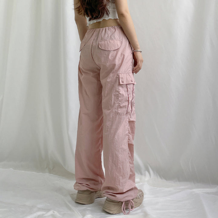 Une femme portant un pantalon cargo rose avec une taille basse et une jambe large. Le pantalon est fini par un élastique à la cheville pour un confort optimal. Disponible du S au L.