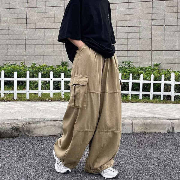 Une femme pose dans la rue avec un tee-shirt noir, des baskets blanches et un pantalon cargo baggy extra-large beige.