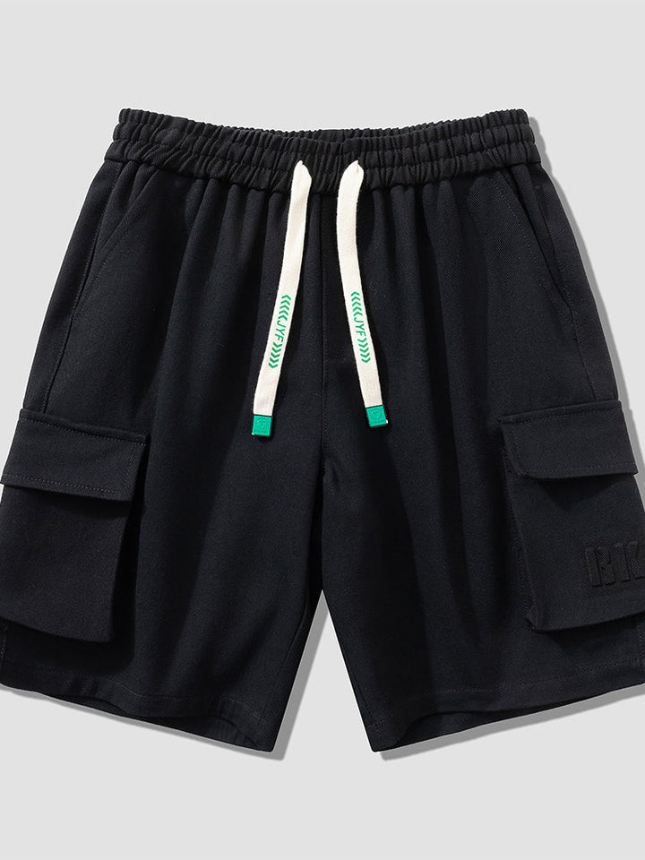 Un short cargo noir pour homme avec une bande blanche et verte. Coupe large, longueur jusqu'aux genoux. Tailles disponibles du M au 8XL. Élastique à la taille avec cordon blanc et turquoise pour ajustement parfait. Conçu en 95% coton et 5% viscose pour douceur, confort et flexibilité. [Cargo District]