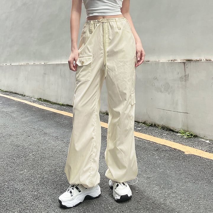 Une personne portant un pantalon blanc baggy avec taille basse élastique pour femme. Fabriqué en polyester et spandex légers, ce pantalon cargo est parfait pour un look street et décontracté. Disponible en blanc cassé du S au L.