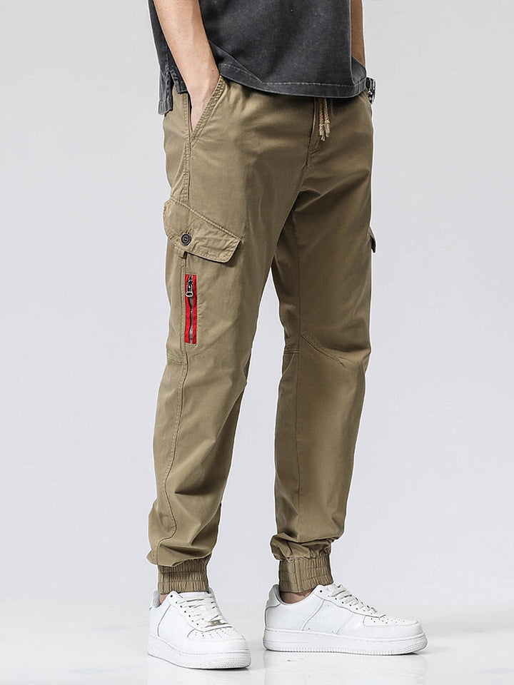 Un homme porte un pantalon cargo coupe droite avec fermeture rouge, couleur vert olive. Le pantalon est en coton et Spandex, alliant douceur, résistance et souplesse. Disponible en tailles US 28-38.