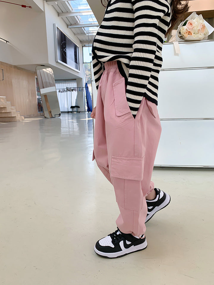 Une personne porte un pantalon cargo jogger large rose. Le pantalon a des poches latérales pratiques et est resserré aux chevilles. Le modèle est disponible du 2 au 7 ans. Confortable et tendance, ce pantalon est fait en coton.