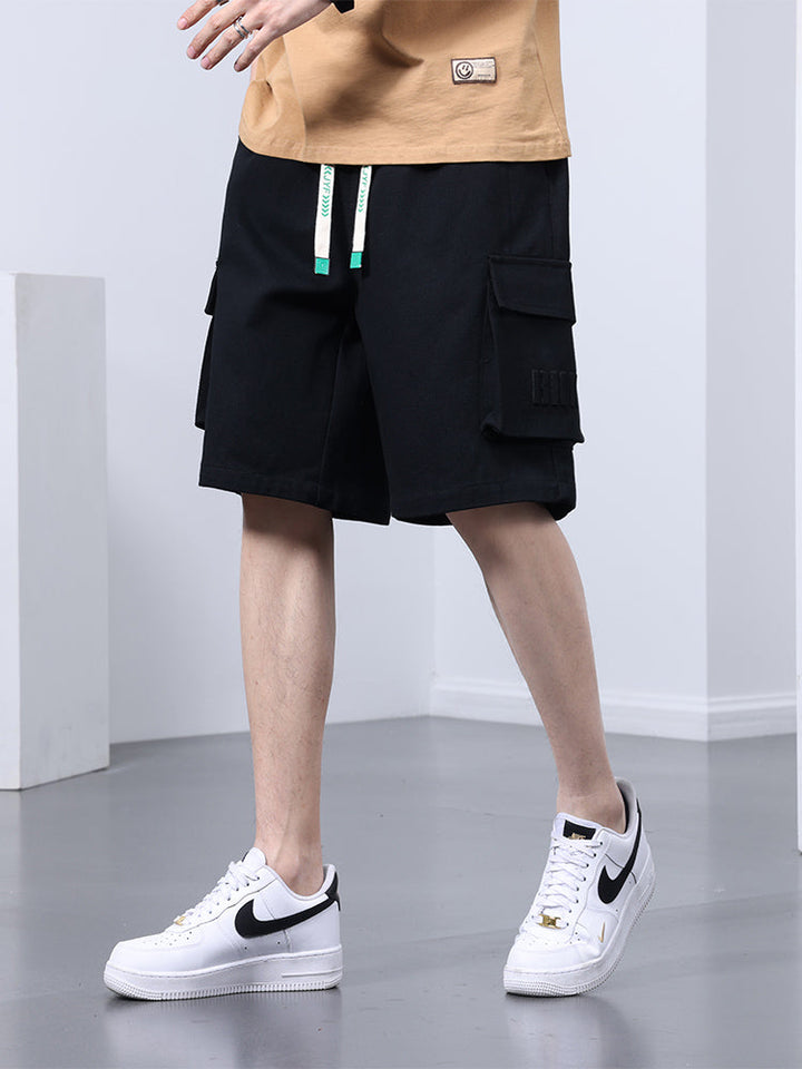 Un homme porte un short cargo noir coupe large avec des sneakers blancs. Le short offre un confort optimal et une grande liberté de mouvement grâce à sa coupe ample et sa longueur jusqu'aux genoux. Disponible du M au 8XL.