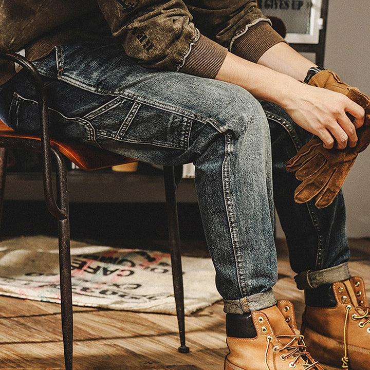 Un homme assis sur une chaise, portant un jean cargo délavé coupe droite bleu. Les petites poches latérales ajoutent une touche tendance à la tenue. Disponible en tailles US du 28 au 40, ce jean en 100% coton offre un confort durable.