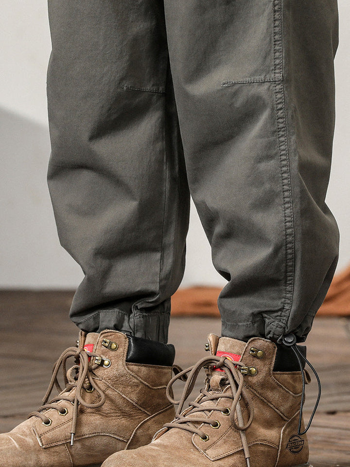 Un homme porte des bottes marron, un pantalon cargo léger ample coupe droite gris pour homme. Les bottes sont visibles dans un plan rapproché. Les détails du pantalon sont décrits dans la description du produit.