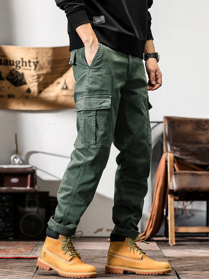 Un homme portant un pantalon cargo gris avec des poches cargo sur les côtés. Coupe droite pour un look masculin intemporel. Disponible en tailles US 28 à 38. Confortable et stylé.