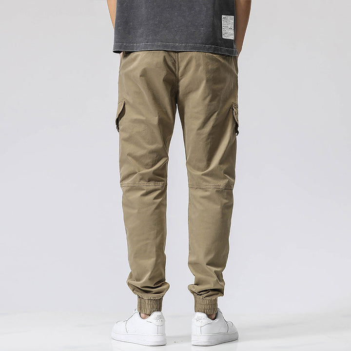 Un homme porte un pantalon cargo coupe droite avec fermeture rouge, de couleur vert olive. Le pantalon est en coton et Spandex, offrant douceur, résistance et souplesse. Disponible dans les tailles 28 à 38.