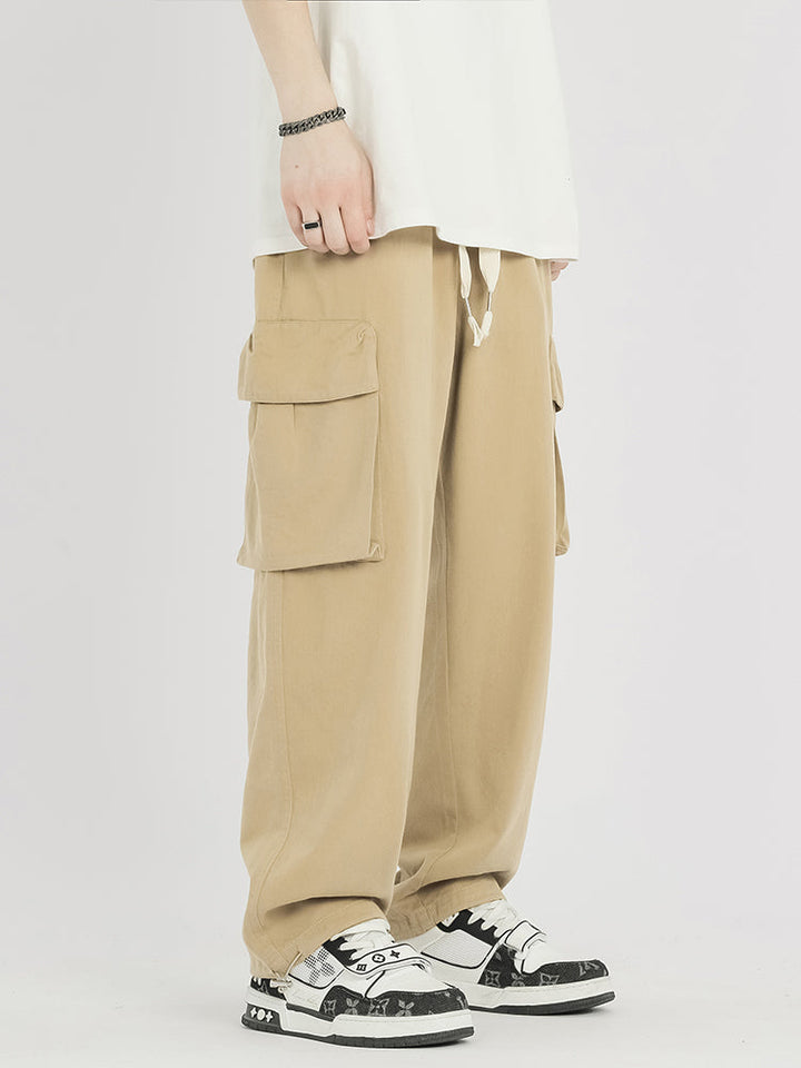 Un homme portant un pantalon cargo baggy en coton beige - Homme. Coupe ample et confortable avec élastique à la taille et aux chevilles. Disponible du S au 2XL.