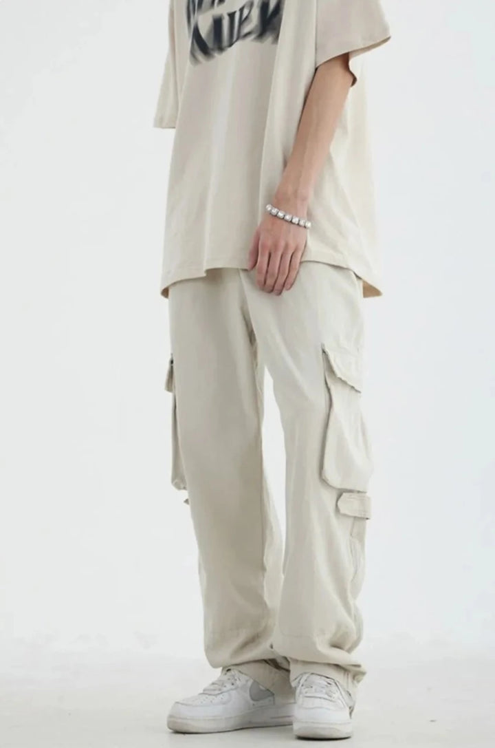 Un homme portant un pantalon cargo blanc avec des poches et une fermeture éclair. Style décontracté et ample, idéal pour un look streetwear japonais vintage. Matière en 100% coton. Disponible en tailles M à 2XL.