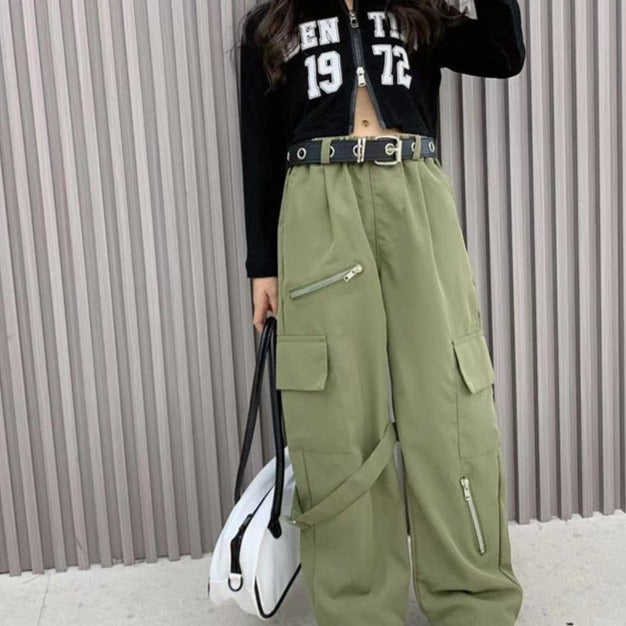 Une femme portant un pantalon cargo baggy kaki avec zip et ceinture.