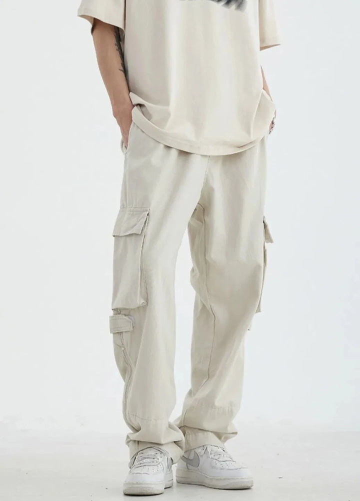 Un homme portant un pantalon blanc cargo HOUZHOU pour homme, style safari décontracté ample, avec poches à fermeture éclair. Matière : 100% coton. Tailles disponibles : M à 2XL.