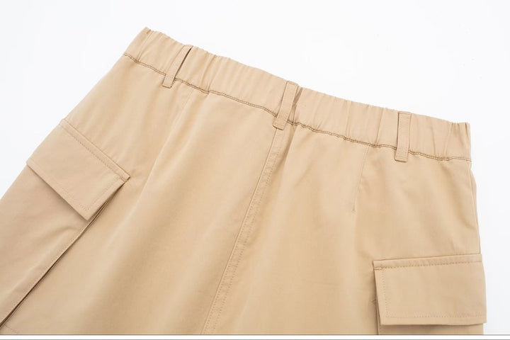 Jupe short cargo beige pour femme - Vue rapprochée d'un tissu beige avec poches cargo dépassant légèrement de la jupe. Hybride élégant d'une mini-jupe évasée et d'un short, disponible en tailles S à XL. Tenue légère et durable en polyester.